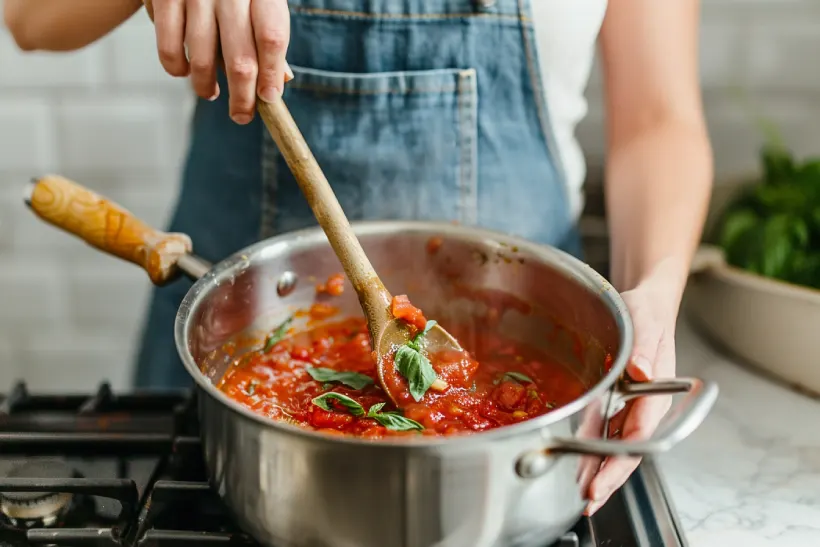 Feminine hand stirring simmering homemade marinara sauce in a saucepan in a bright white kitchen
