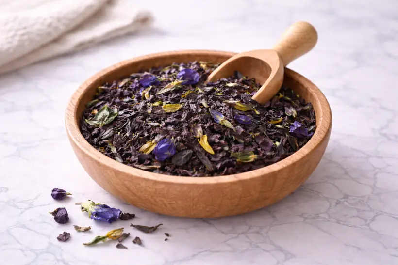 Loose leaf purple tea in a wooden bowl on white marble surface