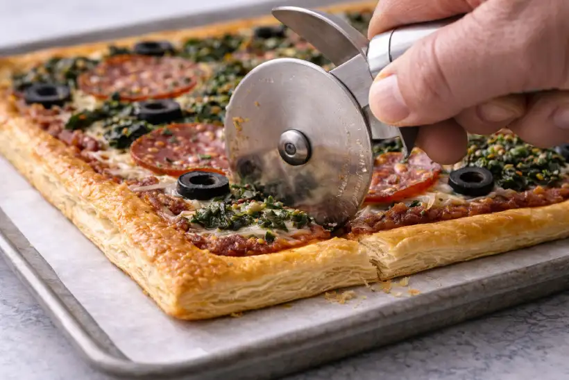 Cutting flaky puff crust pizza with wheel cutter showing layered crust