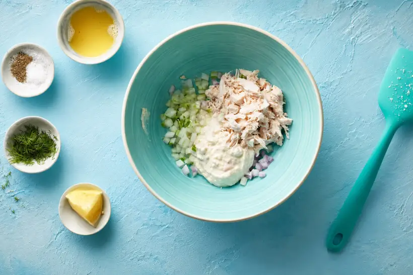 Shredded chicken, Greek yogurt, celery, red onion, and seasonings in a mixing bowl